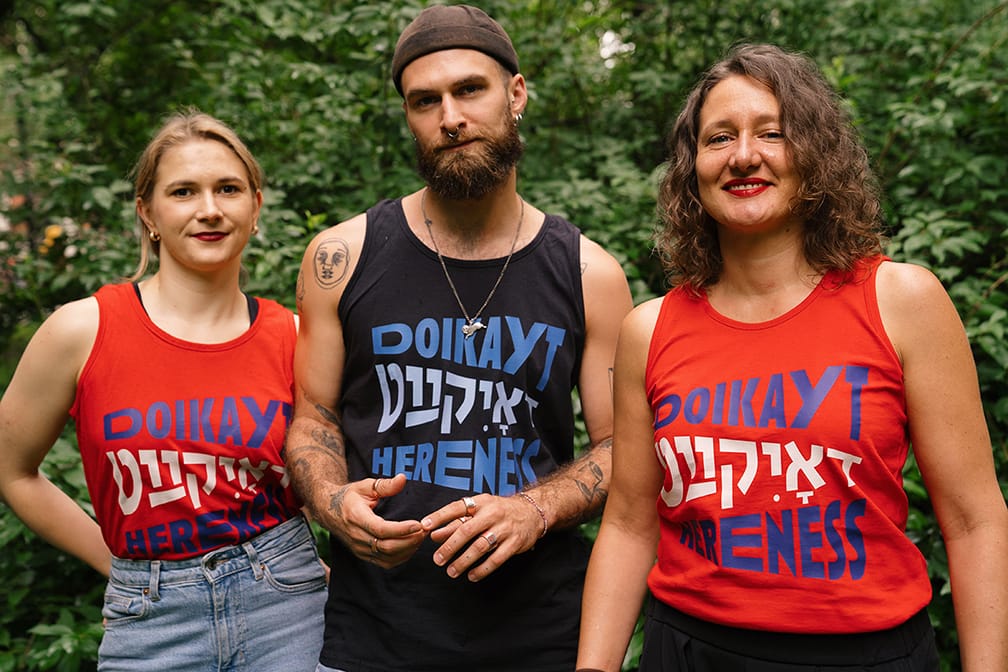 Three models wear red and black shirts reading "doikayt" or "hereness" in English and Yiddish.