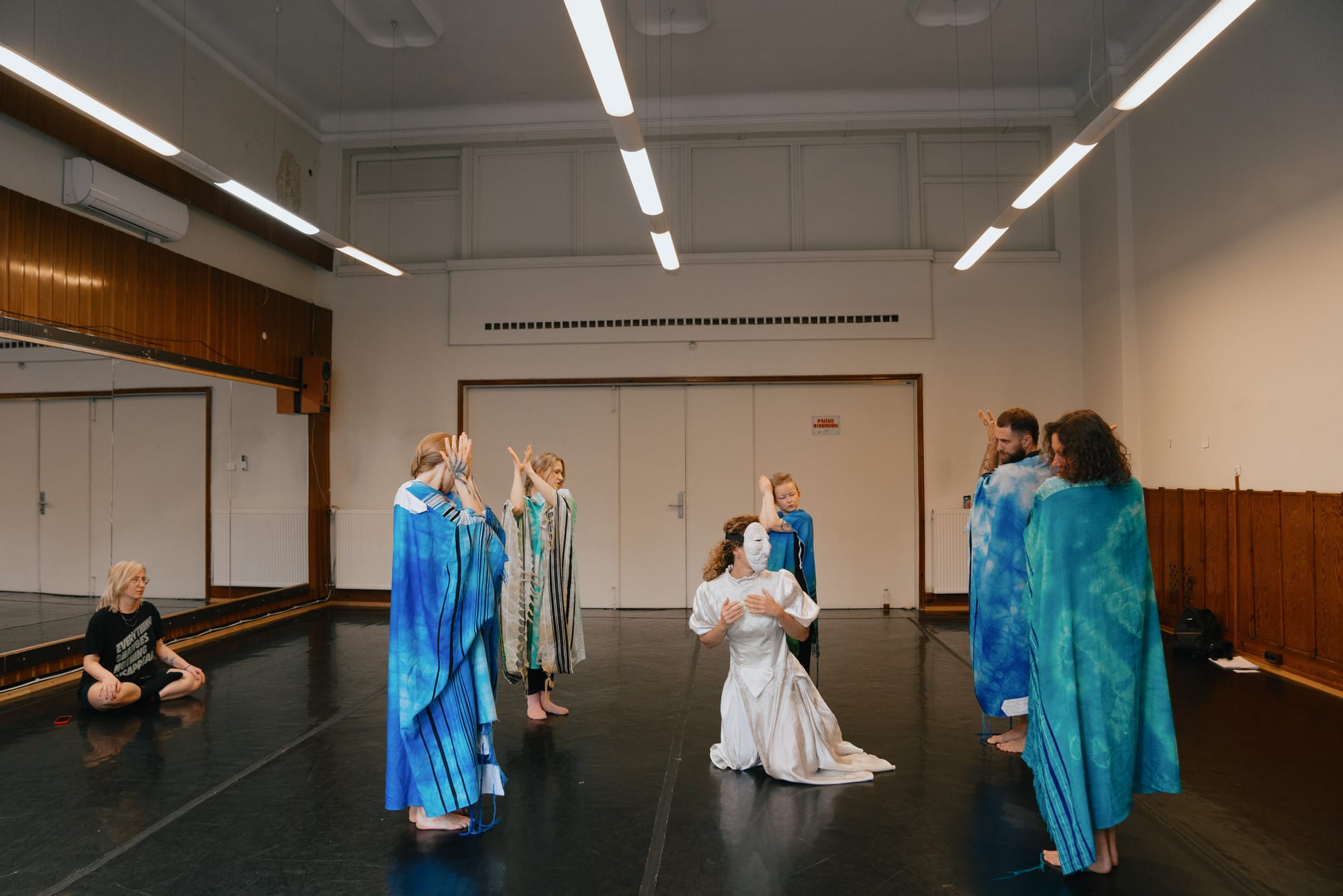 At a performance rehearsal, Weitz kneels in the center of a room as the dybbuk surrounded by dancers shrouded in blue. 