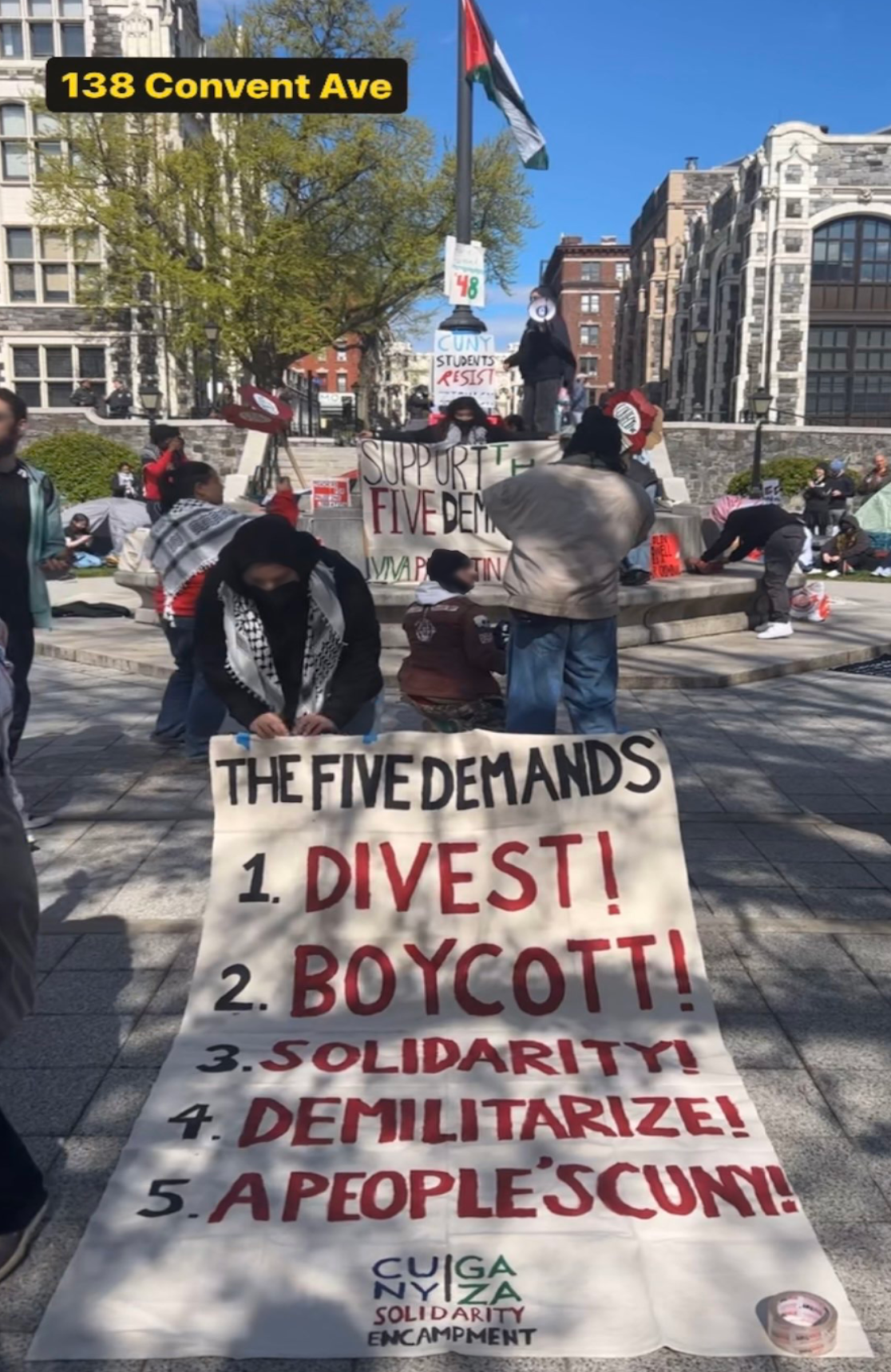 An unfurled banner that reads: The five demands 1. Divest! 2. Boycott! 3. Solidarity! 4. Demilitarize! 5. A people's CUNY