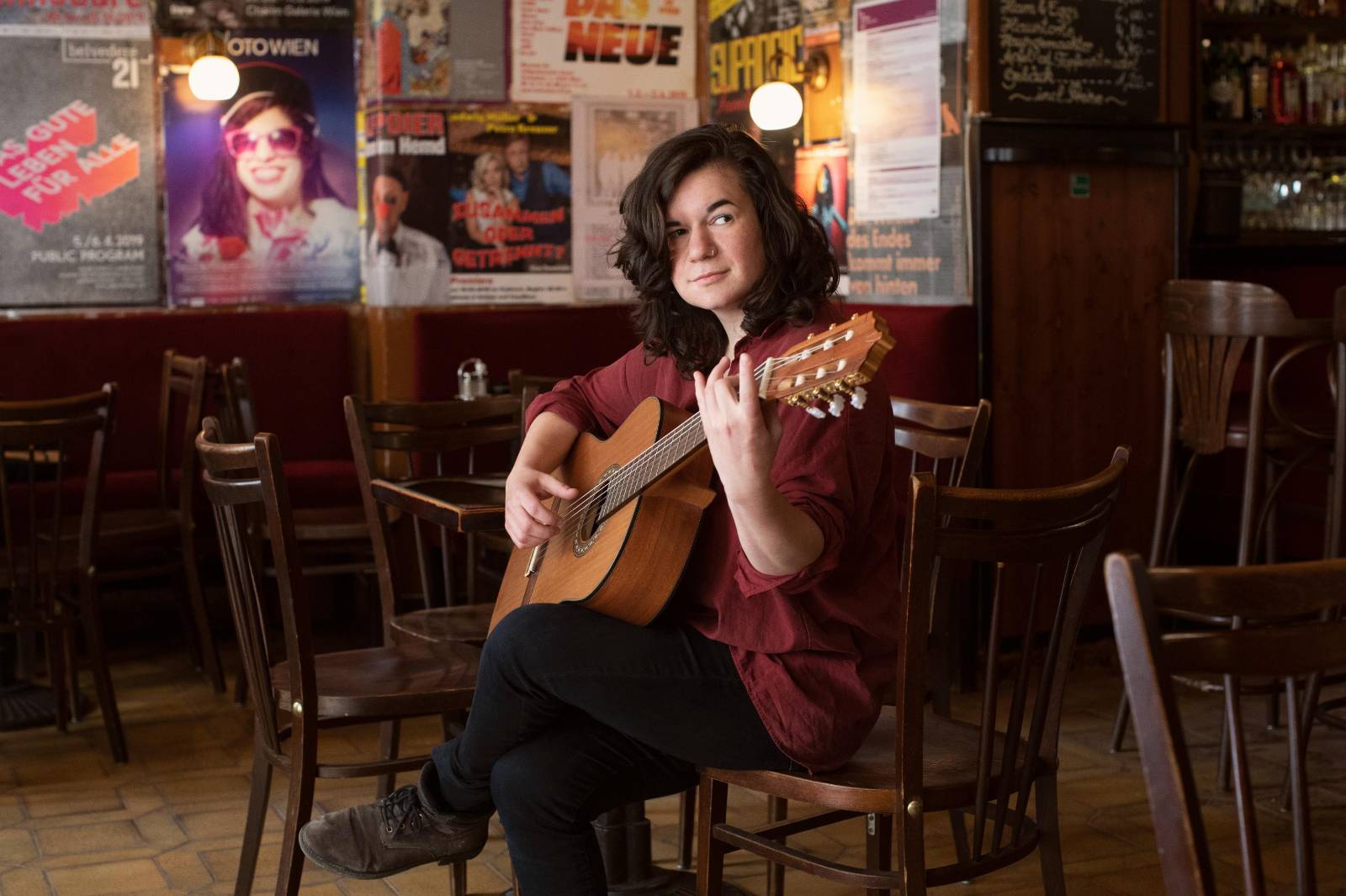 Isabel Frey sits in a cafe holding an acoustic guitar.