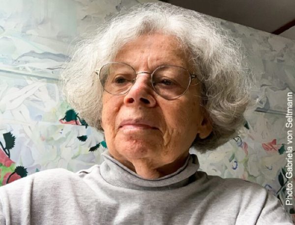 A photo of a woman with glasses and ear length gray hair looking down and to the left. She is wearing a gray turtleneck.