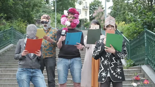 Several people masked in flowers a keffiyeh, and matzoh read from the declaration of independence of diaspora in a park.