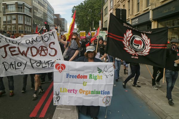 Demonstrators march for migrant rights in London; one banner on the far left reads "fuck racism; Jewdas; daloy politzei."