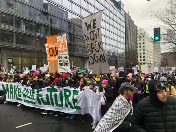 A large crowd holding a banner that reads, "make our future" marches through the street with various protest signs